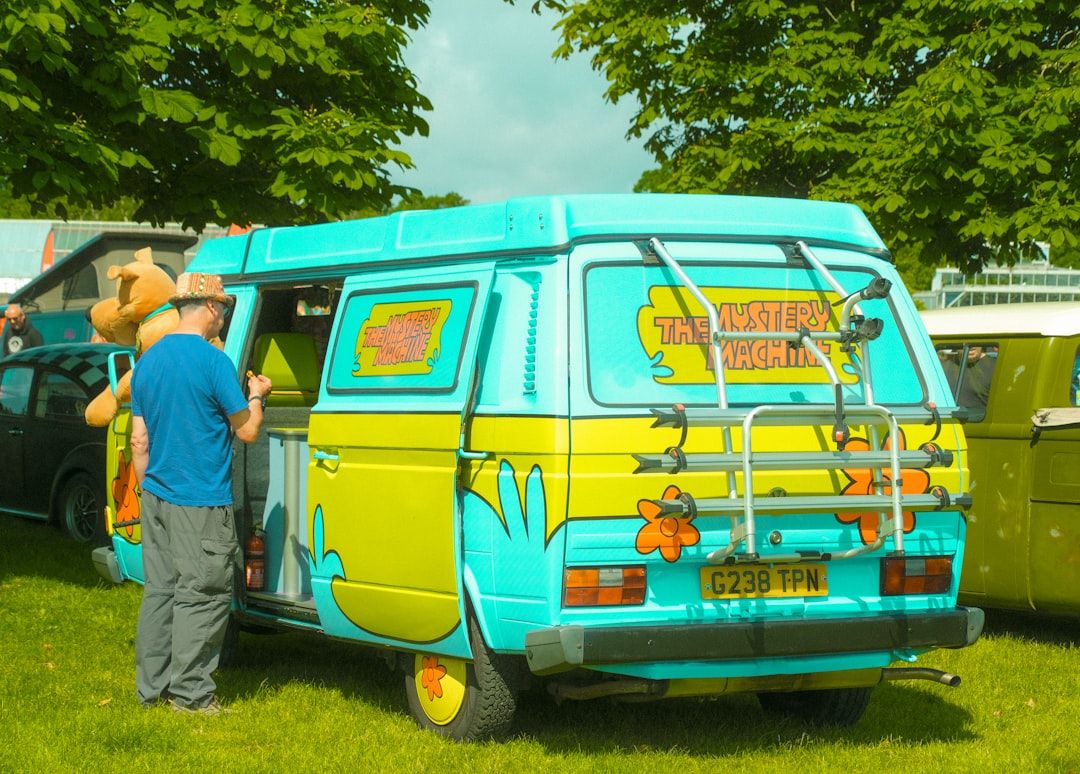 En fargerik festivalbil inspirert av Mystery Machine parkert på gresset.